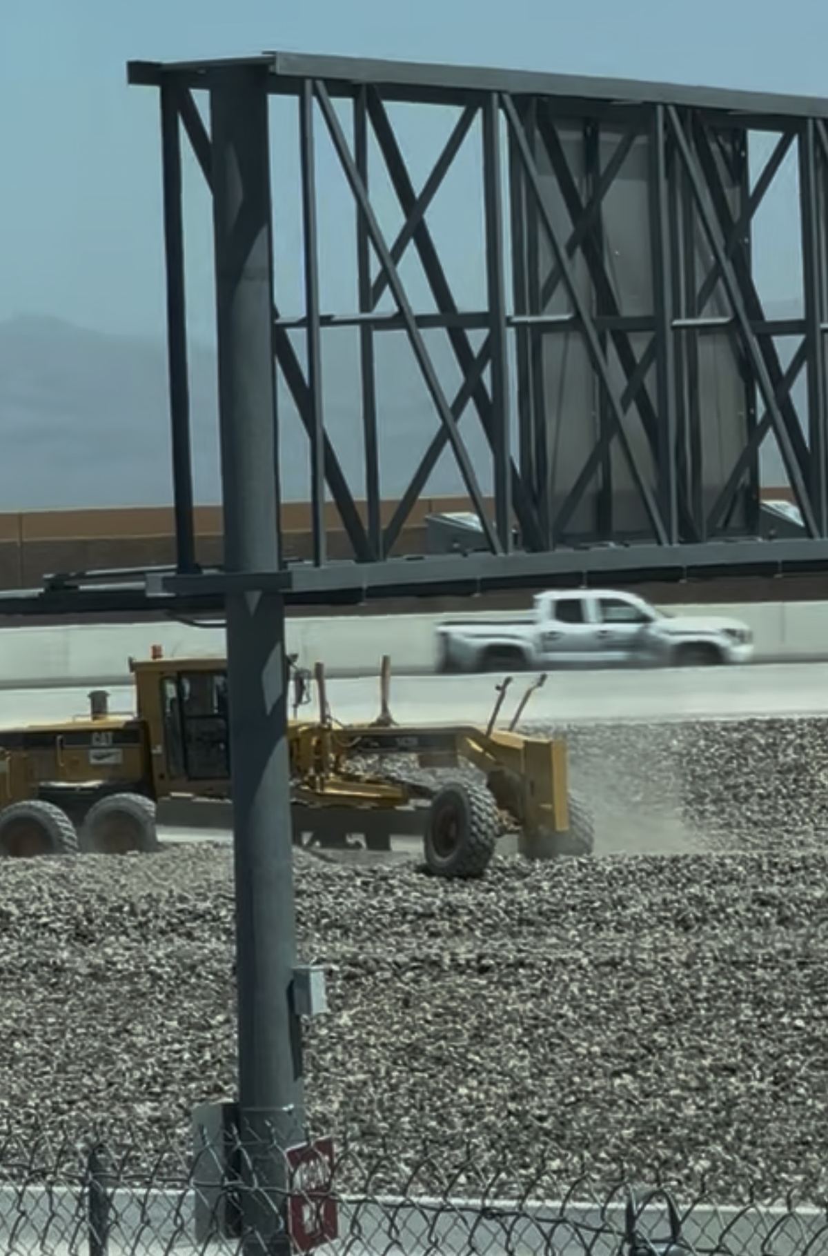 CC-215 construction site with billboard and grader, hazy conditions