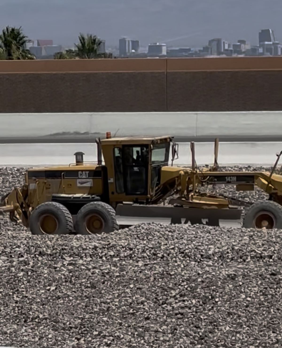 CAT 143H grader close-up with freeway sound wall and Las Vegas skyline
