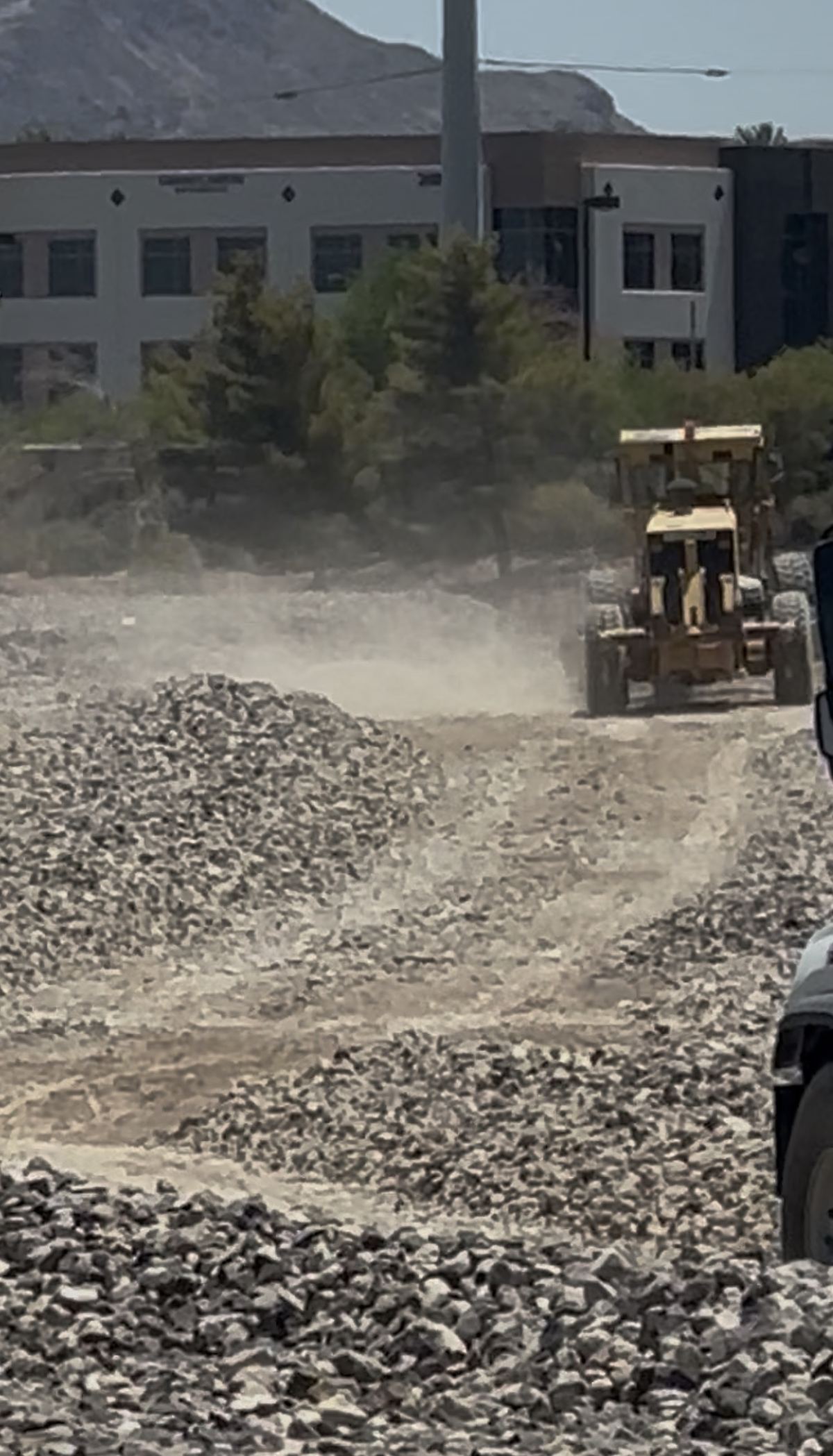CC-215 grader with dust plume, commercial building adjacent