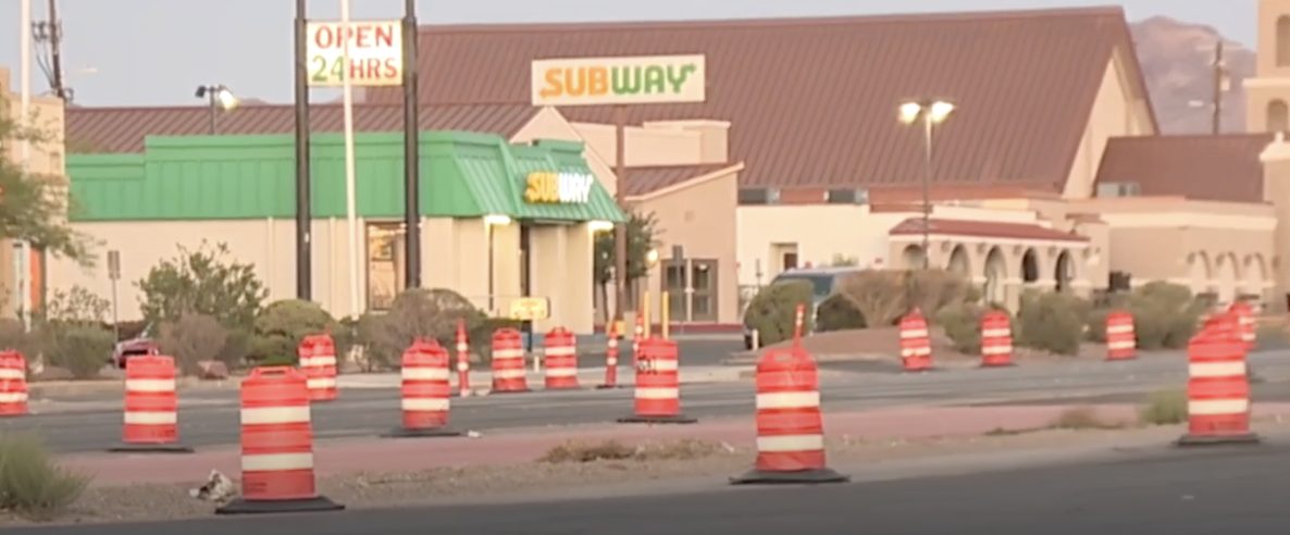 Barrels lining the frontage of businesses along Boulder Highway with disturbed ground between road and storefronts